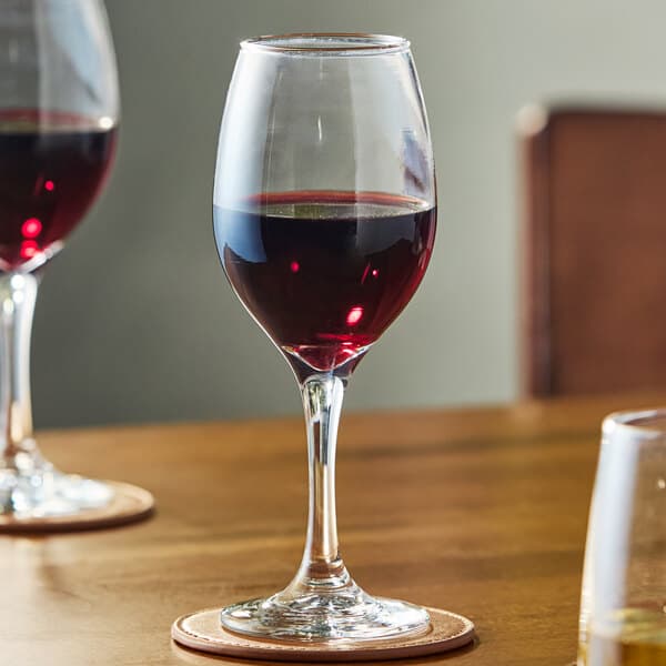 A clear all-purpose wine glass partially filled with red wine, placed on a wooden table.