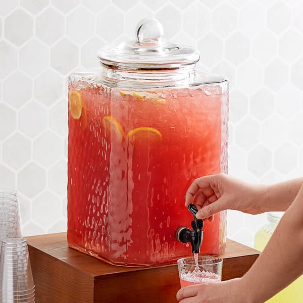 A person pouring a drink from an Acopa glass beverage dispenser.