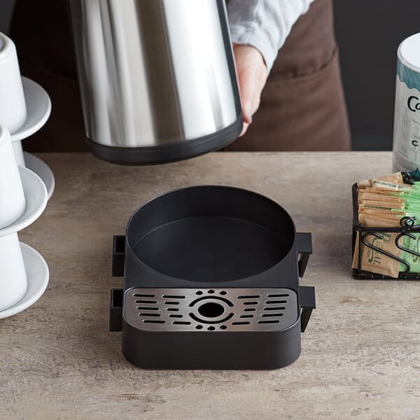 A person pouring coffee into a silver Acopa modular airpot on a wood surface.