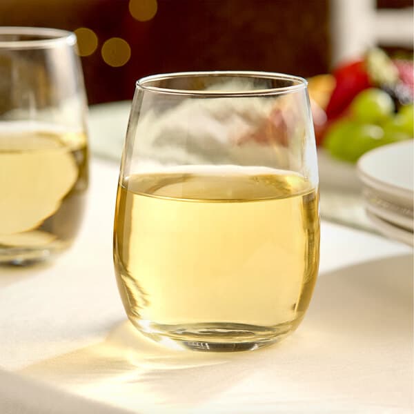 A clear, stemless wine glass filled with white wine, placed on a table.
