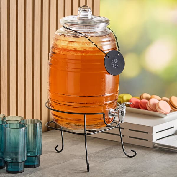 An Acopa glass beverage dispenser filled with iced tea on a table with glasses.