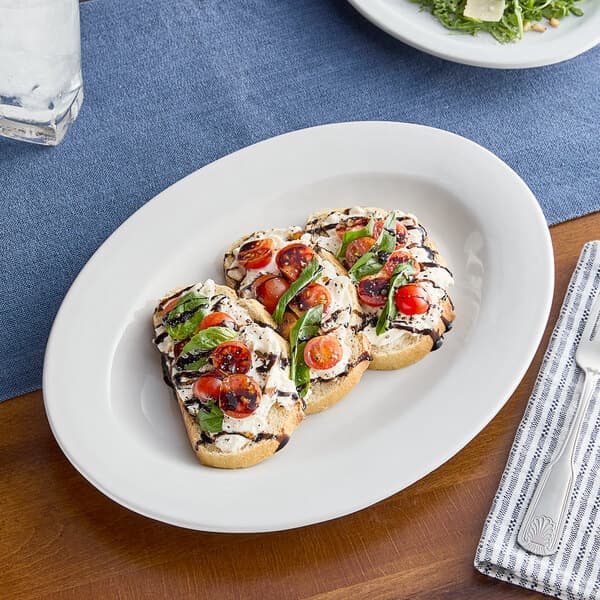 An Acopa Bright White stoneware platter topped with tomatoes, basil, and cheese.