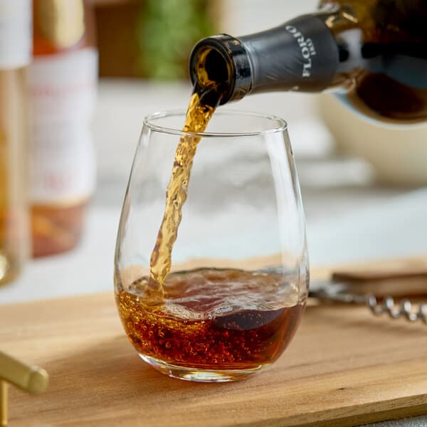 A 12 oz. stemless wine glass being filled with a dark beverage.