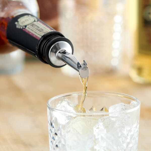 A stainless steel tapered liquor pourer with a flip cap being used to pour liquid into a glass of ice.