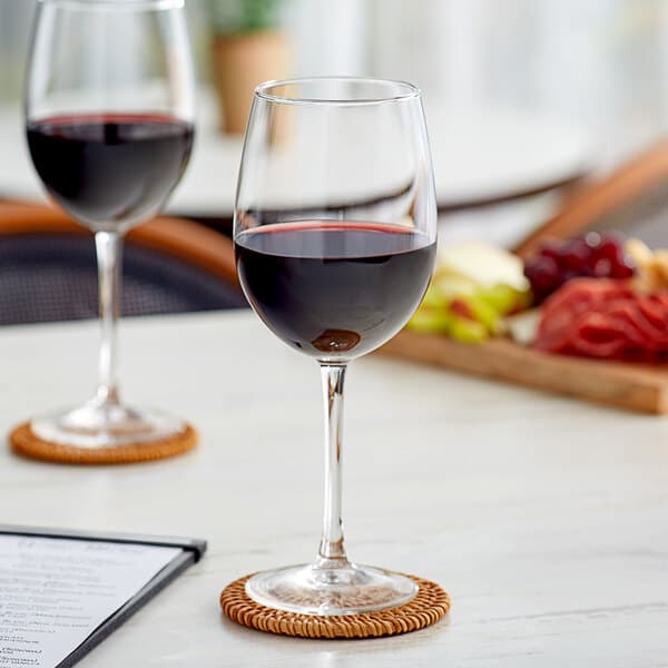 Two Acopa Select Flora wine glasses filled with red wine on a table with food.