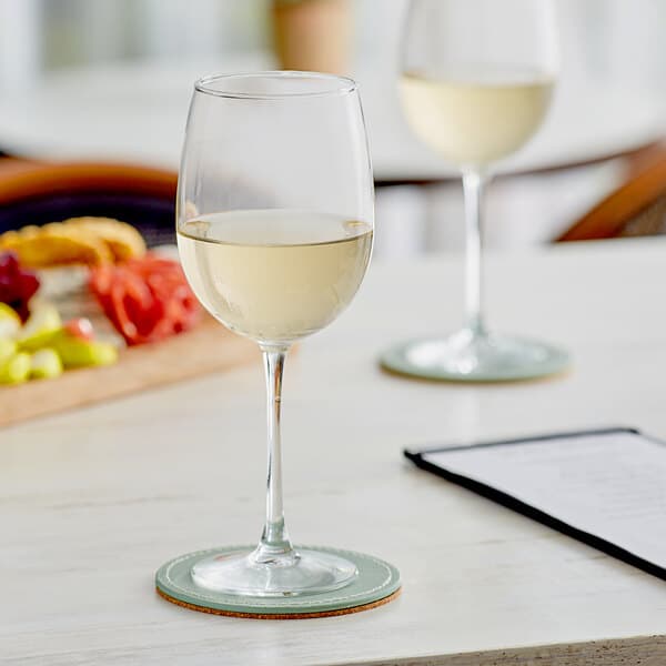 Two Acopa Select Flora wine glasses filled with white wine on a table.