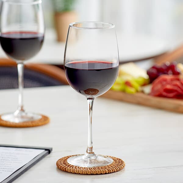 Two Acopa Select Flora wine glasses on a table with a bottle of red wine.