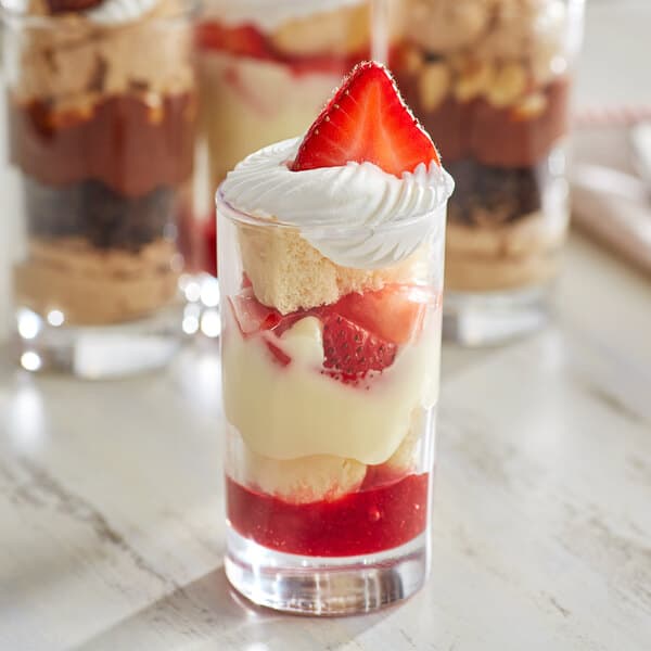 Three Acopa juice glasses filled with dessert and topped with whipped cream and strawberries.