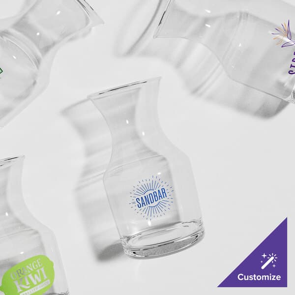 A group of empty clear glass carafes with different logos.