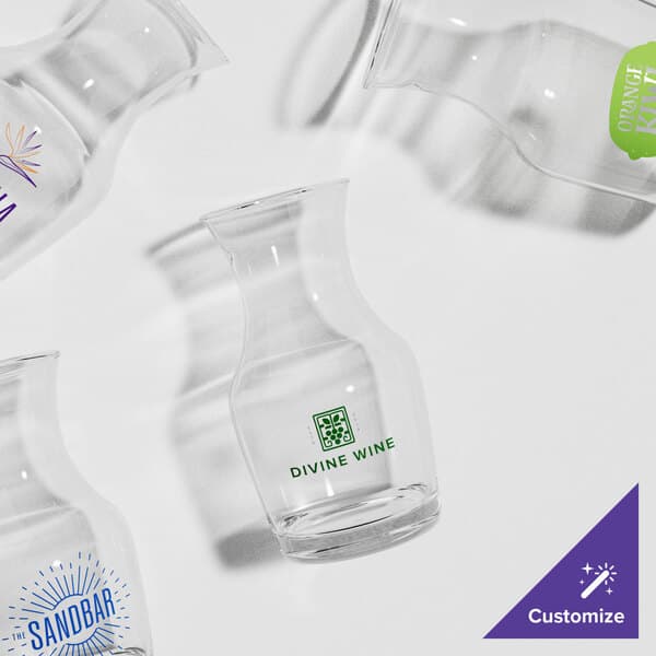 A group of twelve Acopa glass carafes with different logos.