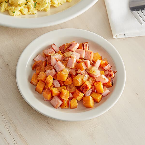 A plate of scrambled eggs with a fork and knife on an Acopa narrow rim stoneware plate on a table.