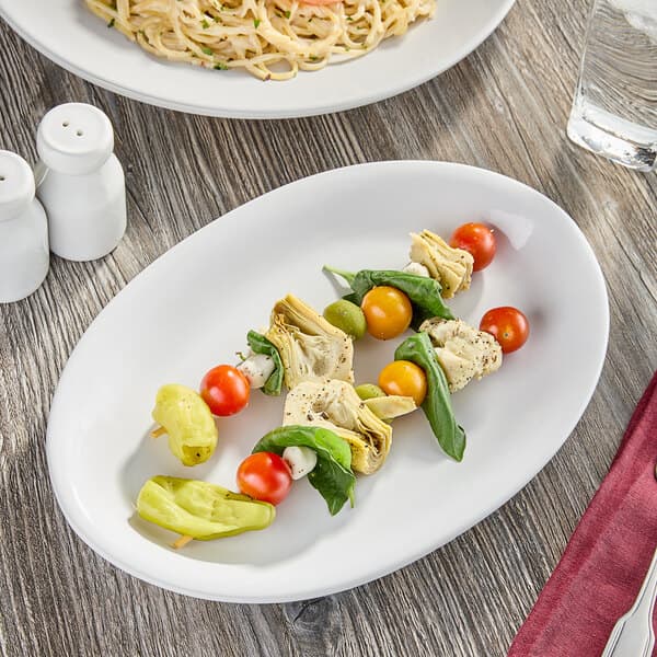An Acopa Bright White oval stoneware platter with food on a table.