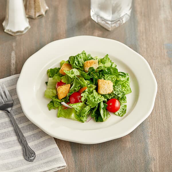 An Acopa ivory stoneware plate with a salad and a fork on a table.