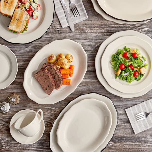 An Acopa ivory stoneware plate with a scalloped edge on a table with plates of meat and vegetables.