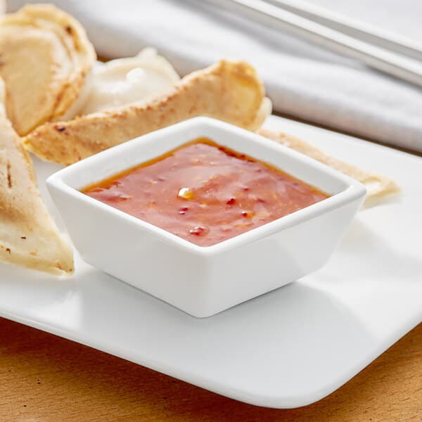 A plate of food with Acopa bright white porcelain sauce cup filled with red sauce on it.