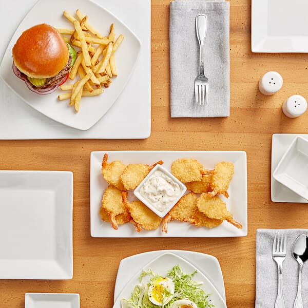 A wood table set with white square Acopa porcelain bowls filled with white sauce and fried chicken nuggets.