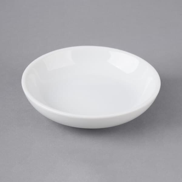 A Choice bright white porcelain round sauce cup on a gray surface.