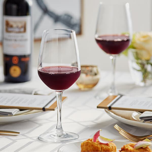 A table with Acopa wine glasses and a glass of red wine on it.