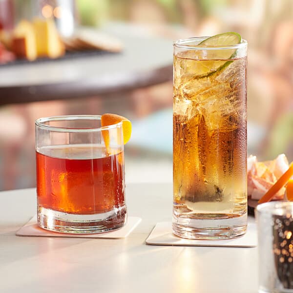 Two Acopa Bermuda beverage glasses with brown liquid and a slice of orange on a table.