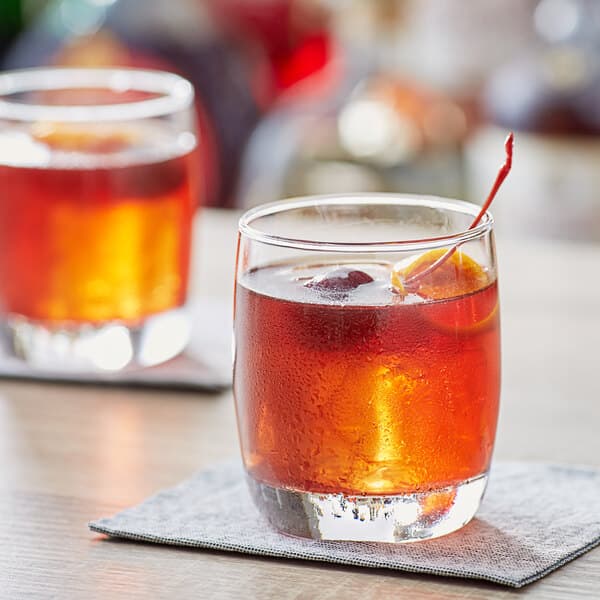 Two Acopa old fashioned glasses of whiskey with orange slices on top.