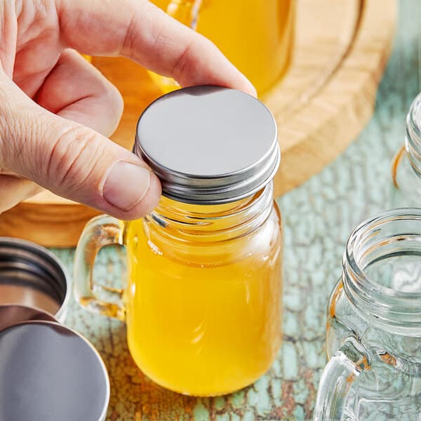 A person holding a small glass jar with a metal lid on it.