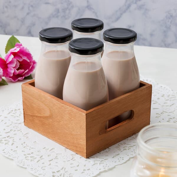 Acopa Black Milk Bottle lids on a group of glass bottles of milk in a wooden crate.