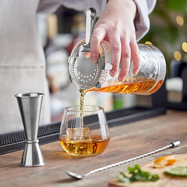 A person using Acopa silver accessories to pour a cocktail into a glass.