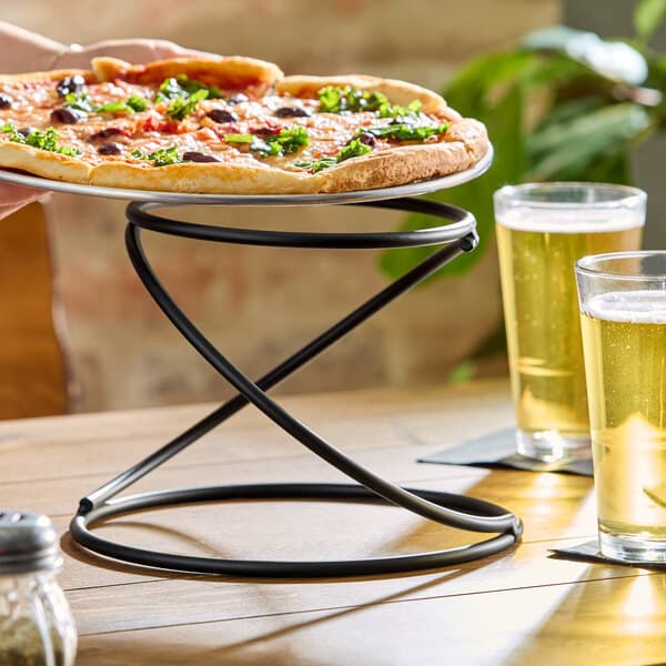 A black metal swirl display stand holding a pizza on a wooden table.