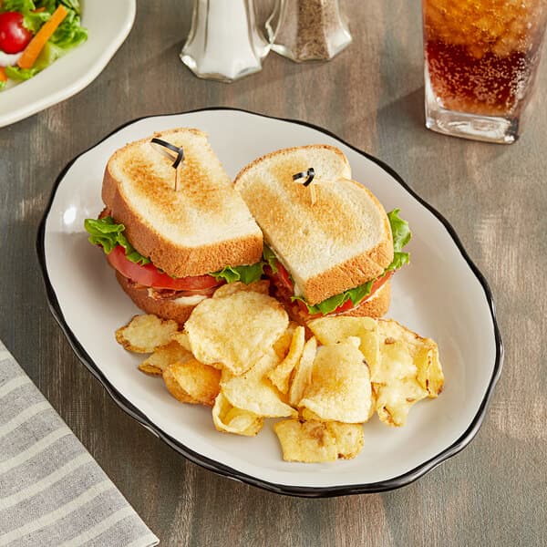 An Acopa ivory stoneware platter with a sandwich, chips, and a drink on it.