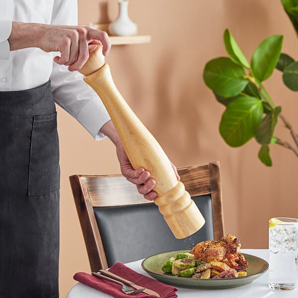 A person using an Acopa wooden pepper mill to grind pepper over a plate of food.