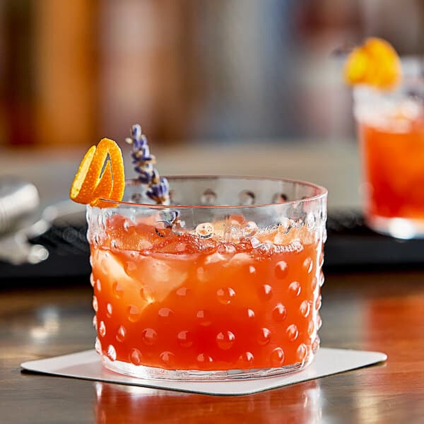 An Acopa hobnail rocks glass with a drink and a slice of orange on the table.
