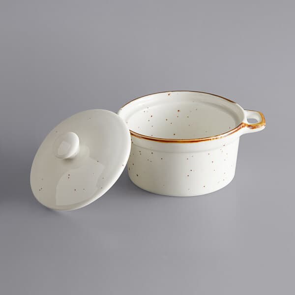 An Acopa Keystone vanilla bean stoneware mini casserole dish with a lid. A white stoneware casserole dish with brown specks.