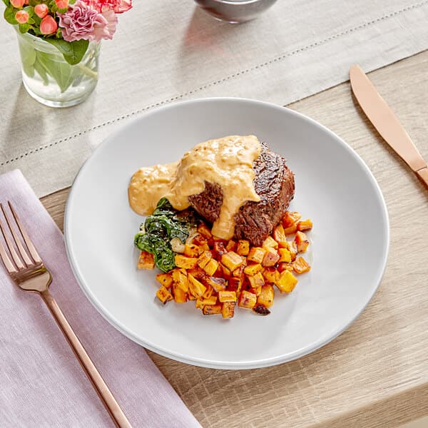 An Acopa matte white stoneware coupe plate with food on a table.