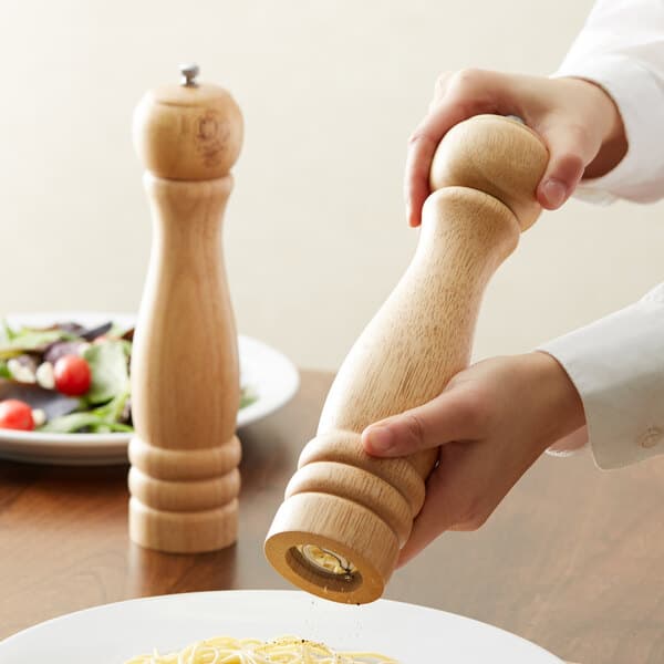 A person using an Acopa wooden pepper mill on a plate of food.