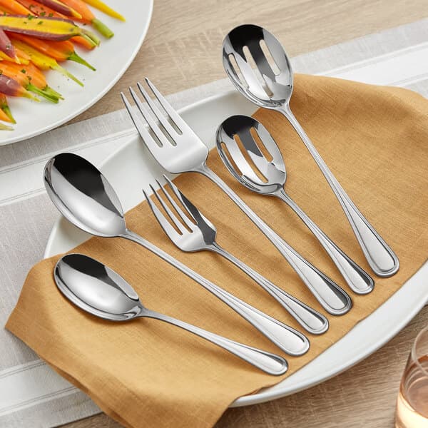 An Acopa Edgeworth stainless steel serving fork on a plate with food and silverware.