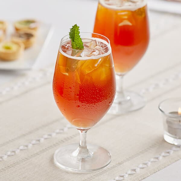 Two Acopa Elevation wine glasses filled with orange liquid and a green leaf on top.