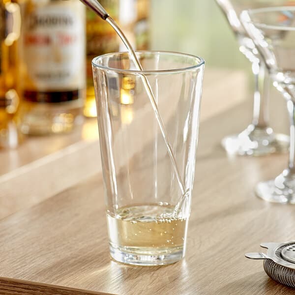 A bottle pouring liquid into an Acopa mixing glass filled with liquid.