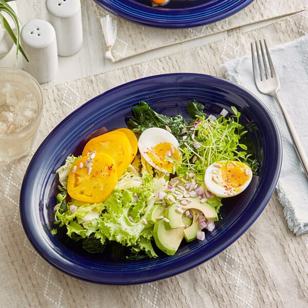 An Acopa Capri deep sea cobalt blue oval stoneware platter with salad, eggs, and avocado.
