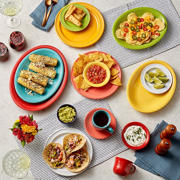 A table in a Mexican restaurant set with colorful Acopa Capri stoneware bowls filled with guacamole, white sauce, and green leaves.