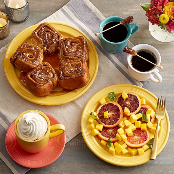 A plate of food and a yellow Acopa Capri stoneware mug filled with coffee on a table.
