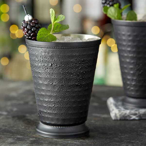 An Acopa matte black metal cup filled with a blackberry bourbon cocktail and ice.