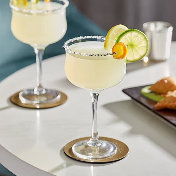 Two Acopa Deco cocktail glasses filled with yellow drinks on a table.