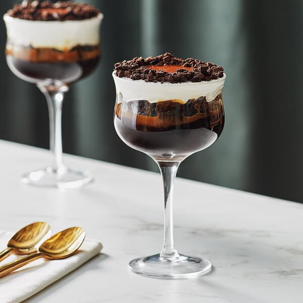 Two Acopa Deco cocktail glasses filled with brown liquid and dessert on a table.