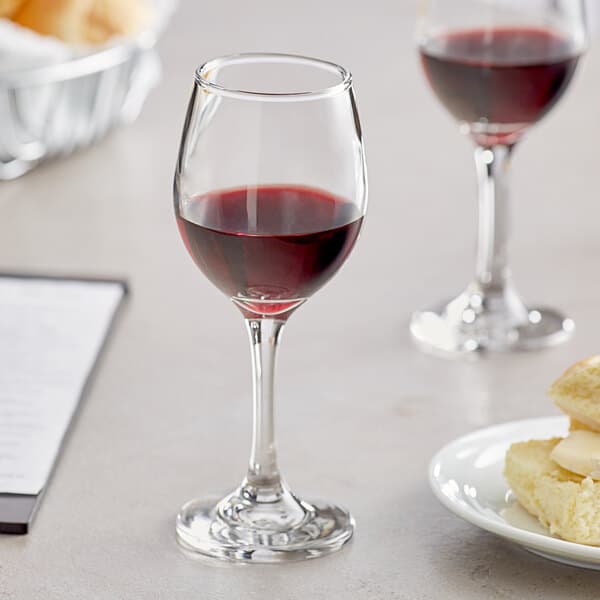 An Acopa wine glass filled with red wine next to a plate of food.