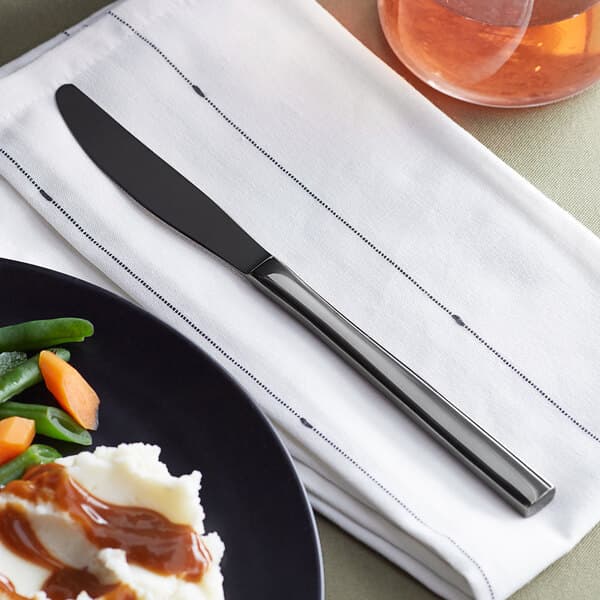 An Acopa Phoenix stainless steel forged dinner knife on a plate of food with mashed potatoes, carrots, and gravy.