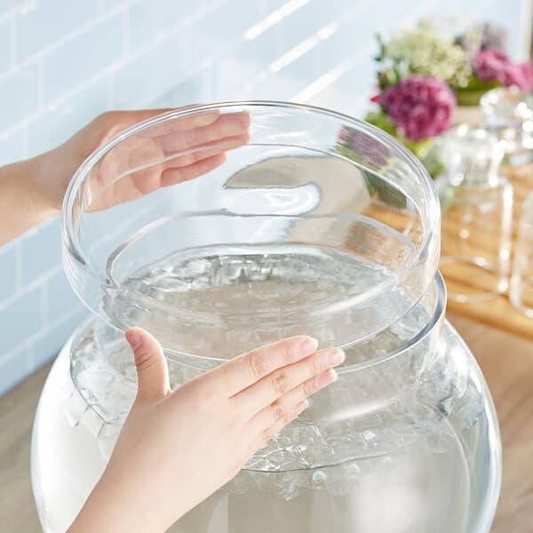 A hand reaching out to the clear glass lid on a large Acopa dispenser.