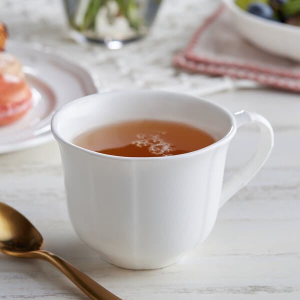 A white Acopa porcelain cup of tea on a table with a gold spoon.