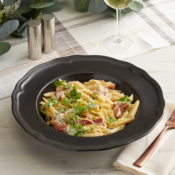 An Acopa Armor Gray porcelain pasta bowl filled with pasta topped with cheese and herbs on a table in an Italian restaurant.