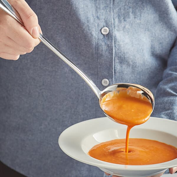 A person using an Acopa stainless steel ladle to pour soup into a bowl.
