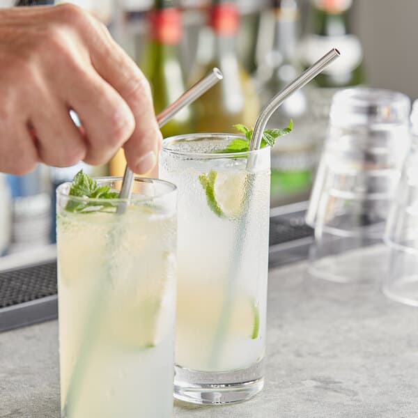 A person holding an Acopa stainless steel bent straw in a glass of liquid.